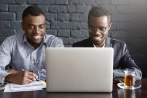 two-cheerful-successful-young-african-american-businessmen-sitting-modern-office-interior-front-open-laptop-computer-looking-screen-with-happy-smiles-discussing-business-plans-ideas_273609-319